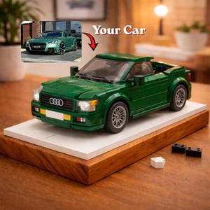 May include: A green toy car model with the text "Your Car" above it. The model is displayed on a white platform set on a wooden base. The car has the Audi logo on the front.