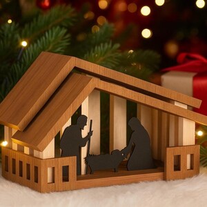 May include: A wooden nativity scene depicting Mary, Joseph, and a lamb within a wooden structure. The roof and base are darker wood, with lighter wood for the walls. The background features a Christmas tree and soft lighting, creating a festive atmosphere.