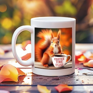Puede incluir: Taza de cerámica blanca con una ardilla roja sosteniendo una taza de café que dice "Coffee Time Best Drink of the Day". La ardilla está sentada sobre una superficie marrón con un fondo borroso de follaje otoñal.