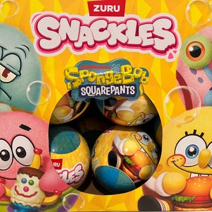 May include: A yellow box of ZURU Snackles featuring SpongeBob SquarePants characters. The box includes images of SpongeBob, Patrick, Squidward, and Gary. The box contains several round, colorful containers with SpongeBob designs.
