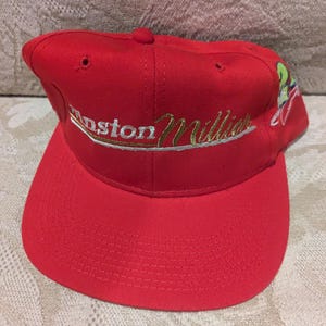 May include: A red baseball cap with a white and gold embroidered logo that says "Winston Miller" on the front. The cap has a curved brim and a mesh back.