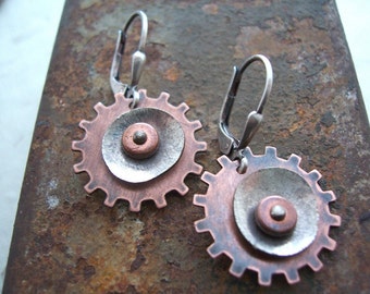 Peut inclure: Une paire de boucles d'oreilles en argent et cuivre en forme d'engrenages avec un motif circulaire au centre. Les boucles d'oreilles ont une fermeture à crochet.