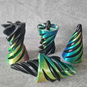 May include: Four 3D printed objects with a spiral design. The objects are black with iridescent green and blue accents.