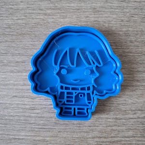 May include: A bright blue cookie cutter in the shape of a cartoon person with short hair and a smiling face. The cutter has a detailed design of the person's clothing and facial features.