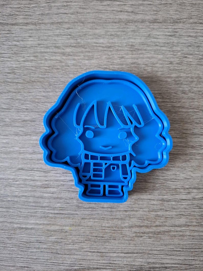 May include: A bright blue cookie cutter in the shape of a cartoon person with short hair and a smiling face. The cutter has a detailed design of the person's clothing and facial features.