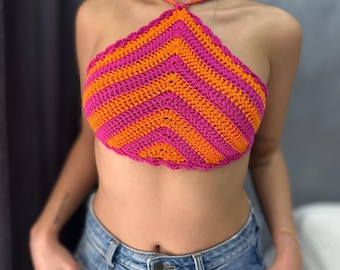 May include: A handmade crochet halter top in a vibrant chevron pattern. The top features alternating stripes of bright orange and hot pink. The halter straps are a matching orange and pink. The top is worn with blue jeans.