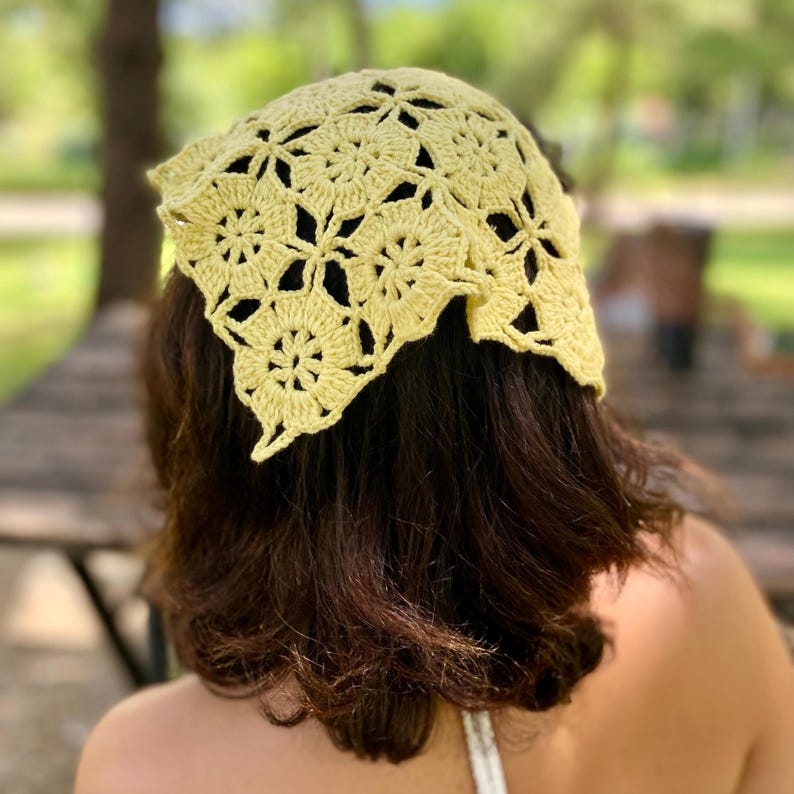 May include: A light yellow crochet headscarf with a floral pattern. The head covering is made of a soft, open-weave material. The headscarf is worn on the head and covers the top of the head and the back of the hair.