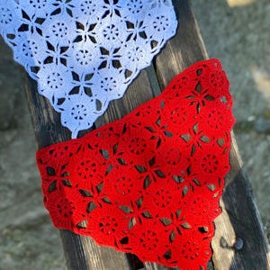 May include: Two crocheted doilies, one white and one red, are displayed on a wooden surface. The doilies feature a floral pattern with openwork details. The red doily is in the foreground, with the white doily partially visible above.