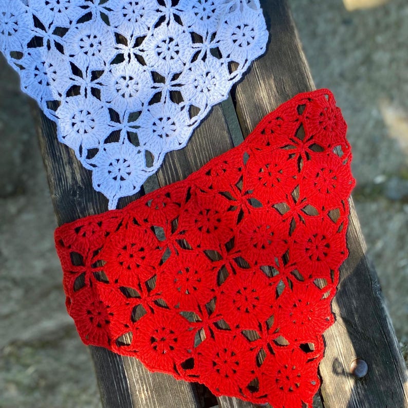 May include: Two crocheted doilies, one white and one red, are displayed on a wooden surface. The doilies feature a floral pattern with openwork details. The red doily is in the foreground, with the white doily partially visible above.