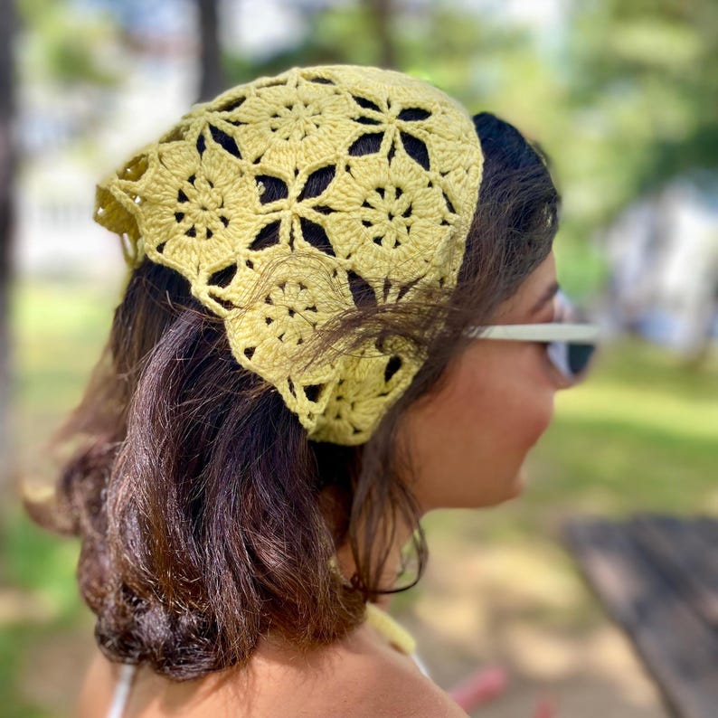 May include: A light yellow crochet headscarf with a floral pattern. The headscarf is worn on the head and covers the hair. The crochet work is detailed and the color is a soft, muted yellow.