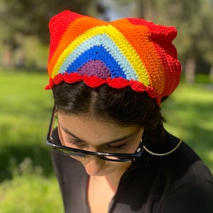 Könnte beinhalten: Ein Regenbogen-Stirnband aus Häkelarbeit mit einem gewellten Rand. Das Stirnband ist aus buntem Garn gefertigt und hat ein Regenbogenmuster.