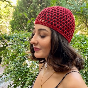 May include: A red crocheted beanie hat with a grid-like pattern. The hat is made of a soft, textured yarn and is worn on the head. The hat is a stylish accessory for any outfit.