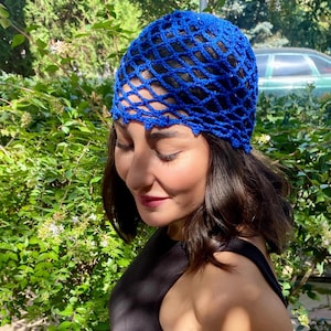 May include: A vibrant blue crocheted hat with an open, net-like design. The hat is made of a shiny, possibly metallic yarn, and is worn on the head. The hat is a bright, eye-catching accessory.