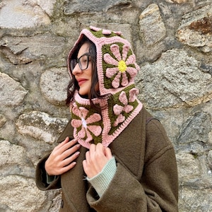 May include: A handmade crochet hood and cowl set. The hood and cowl are made with pink, green, and yellow yarn, featuring a daisy flower design. The hood and cowl are designed to be worn together.