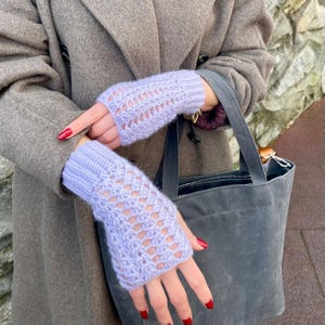 May include: Pale lilac fingerless gloves with a detailed openwork pattern. The gloves are made from a soft, knitted fabric. The gloves are displayed against a neutral backdrop.