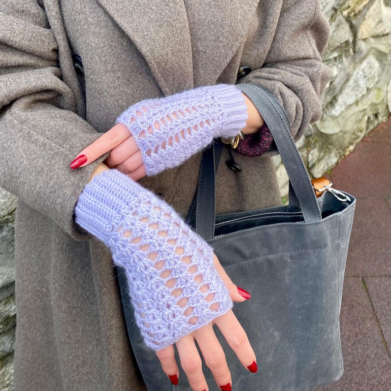 May include: Pale lilac fingerless gloves with a detailed openwork pattern. The gloves are made from a soft, knitted fabric. The gloves are displayed against a neutral backdrop.