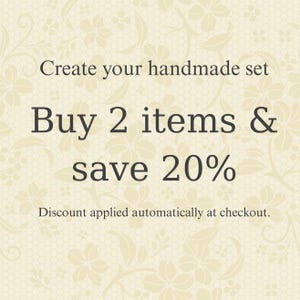 May include: Cream-colored background with a floral lace pattern. Text in a dark brown font reads "Create your handmade set. Buy 2 items & save 20%." Additional text states "Discount applied automatically at checkout."