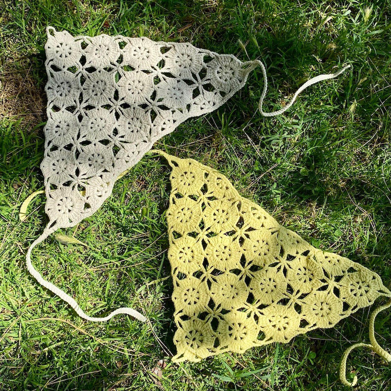 May include: Two handmade crochet tops in the image. One is a light beige color, and the other is a pale yellow-green. Both tops have a floral pattern and long ties. The tops are lying on green grass.