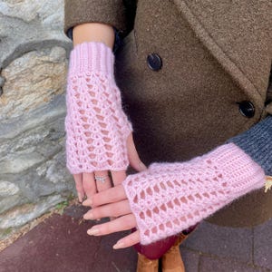 May include: Pale pink, open-weave fingerless gloves. The gloves are knitted with a soft yarn and feature a ribbed cuff. The open design allows for finger movement while keeping the hands warm. A stylish accessory.