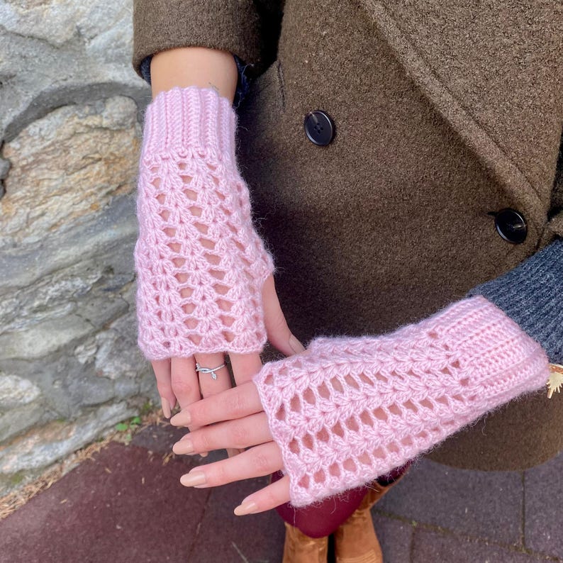 May include: Pale pink, open-weave fingerless gloves. The gloves are knitted with a soft yarn and feature a ribbed cuff. The open design allows for finger movement while keeping the hands warm. A stylish accessory.