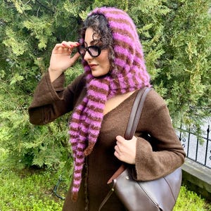 Puede incluir: Bufanda con capucha a rayas moradas y marrones, usada con un su&eacute;ter marr&oacute;n y un bolso marr&oacute;n. La persona lleva gafas negras. Accesorio de moda.