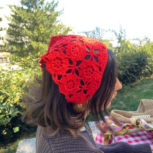 May include: A vibrant red crochet headband featuring a floral pattern. The openwork design allows glimpses of the hair beneath. This handmade accessory adds a pop of color and a touch of bohemian flair.