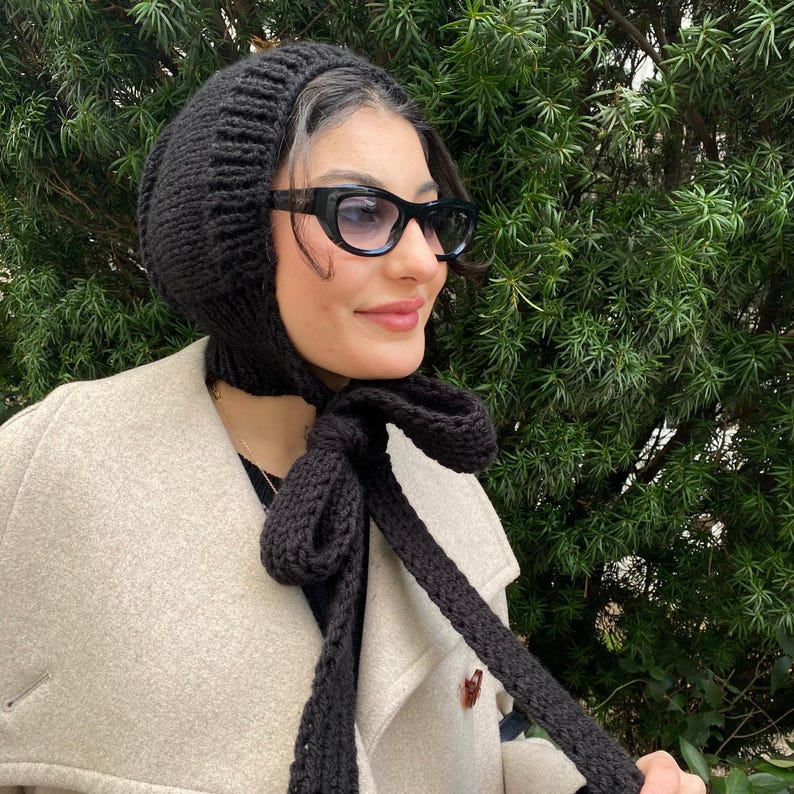 May include: A black knitted hat with a matching scarf. The hat has a long, pointed flap that can be tied at the neck. The scarf is tied in a bow at the front.