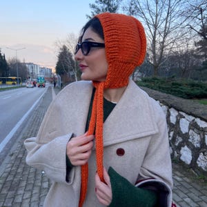 May include: A bright orange knitted hat with a long matching scarf. The hat has a pointed top and the scarf is tied around the neck.