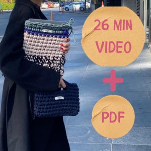 May include: A person holding a large, multi-colored crocheted laptop sleeve and a small, navy blue crocheted handbag. The laptop sleeve features green, blue, beige, and black sections. The image also includes text that says "26 MIN VIDEO + PDF".