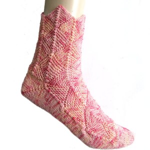 Op de afbeelding: Roze en crèmekleurige gebreide sokken met een geometrisch patroon. De sokken zijn enkelhoog en hebben een gegolfde bovenkant.