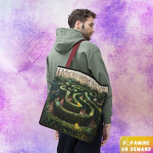 May include: A green tote bag with a red handle and a printed design of a maze with the text "Living in a constant plot twist".