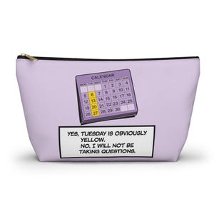 May include: A purple zippered pouch with a calendar graphic and the text "YES, TUESDAY IS OBVIOUSLY YELLOW. NO, I WILL NOT BE TAKING QUESTIONS."