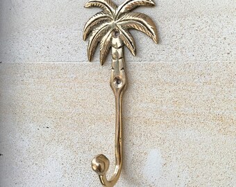 Puede incluir: Un gancho de metal dorado con forma de palmera. El gancho es de metal y tiene un diseño simple. Es perfecto para colgar toallas, batas u otros artículos en un baño o dormitorio.