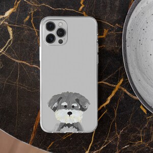 May include: Clear phone case featuring a hand-painted illustration of a Schnauzer dog. The dog has gray fur, a white beard, and a black nose. The case is on a dark, marble-like surface.