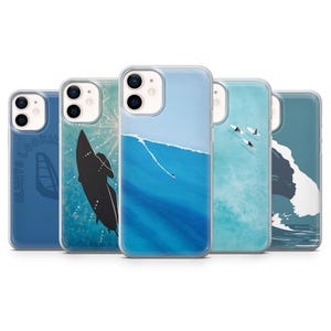 Puede incluir: Una colección de cinco fundas para teléfono con diseños temáticos del océano. Las fundas presentan ilustraciones de surf, olas y el texto "ALWAYS LOOKIN". La paleta de colores incluye tonos de azul, blanco y negro, creando una estética costera.