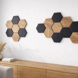 Puede incluir: Dos conjuntos de arte mural hexagonal. Uno tiene forma de flor y el otro es más largo. Las piezas están hechas de hexágonos negros y de madera alternados. La pared es blanca y los muebles son de madera.