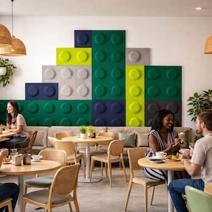 May include: A cafe interior with people seated at round tables. The wall features large, colorful, Lego-like panels in shades of green, blue, gray, and yellow. Wicker lamps hang from the ceiling, and plants add a natural touch to the space.