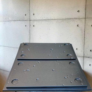 Könnte beinhalten: Zwei schwarze rechteckige Metalltabletts mit einer strukturierten Oberfläche und mehreren runden Löchern. Die Tabletts sind übereinander gestapelt.