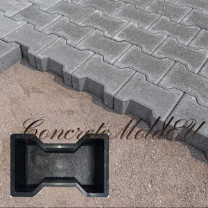 May include: Black plastic mold for making concrete pavers. The mold is shaped like a brick with a curved top and bottom. The mold is sitting on a bed of gravel.