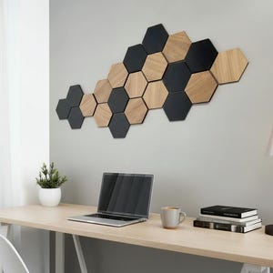 May include: A wall-mounted decorative art piece composed of hexagonal wooden tiles in black and natural wood tones. The tiles are arranged in a geometric pattern. A laptop, mug, and books sit on a light wood desk.