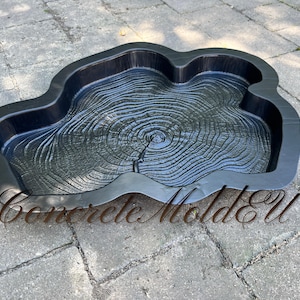 May include: Black plastic mould for making concrete stepping stones. The mould is shaped like a tree stump with concentric rings.