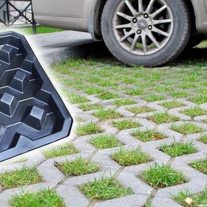 Puede incluir: Un molde de plástico negro para crear adoquines de césped. El molde tiene un patrón de cuadrícula con 12 depresiones cuadradas. El molde se muestra junto a un automóvil estacionado en un camino de entrada hecho de adoquines de césped.