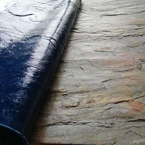 以下が含まれることがあります： 濃い青色のテクスチャのあるビニールシートのクローズアップ。シートは部分的に巻き上げられており、その下にある薄い灰色のテクスチャのあるスレートのような表面が露出しています。