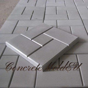 Può includere: Un primo piano di uno stampo in cemento grigio per la realizzazione di pavé autobloccanti. Lo stampo è realizzato in un materiale resistente e ha una superficie liscia. Lo stampo è progettato per creare pavé con un motivo unico.