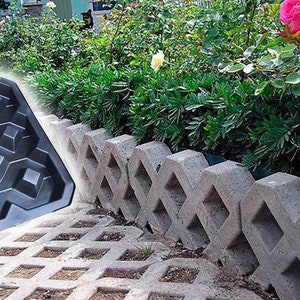Puede incluir: Un molde de plástico negro con un patrón de cuadrícula de indentaciones cuadradas. El molde está sentado en un patio de concreto gris con un borde decorativo de bloques de concreto gris.