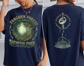 May include: Navy blue t-shirt featuring a Fangorn Forest National Park design on the front, with a forest scene and text. The back displays a design with a ring, sword, and silhouette of a city. The shirt includes the text "HOME OF THE ENTS FOR TREE, ROOT AND TWIG."