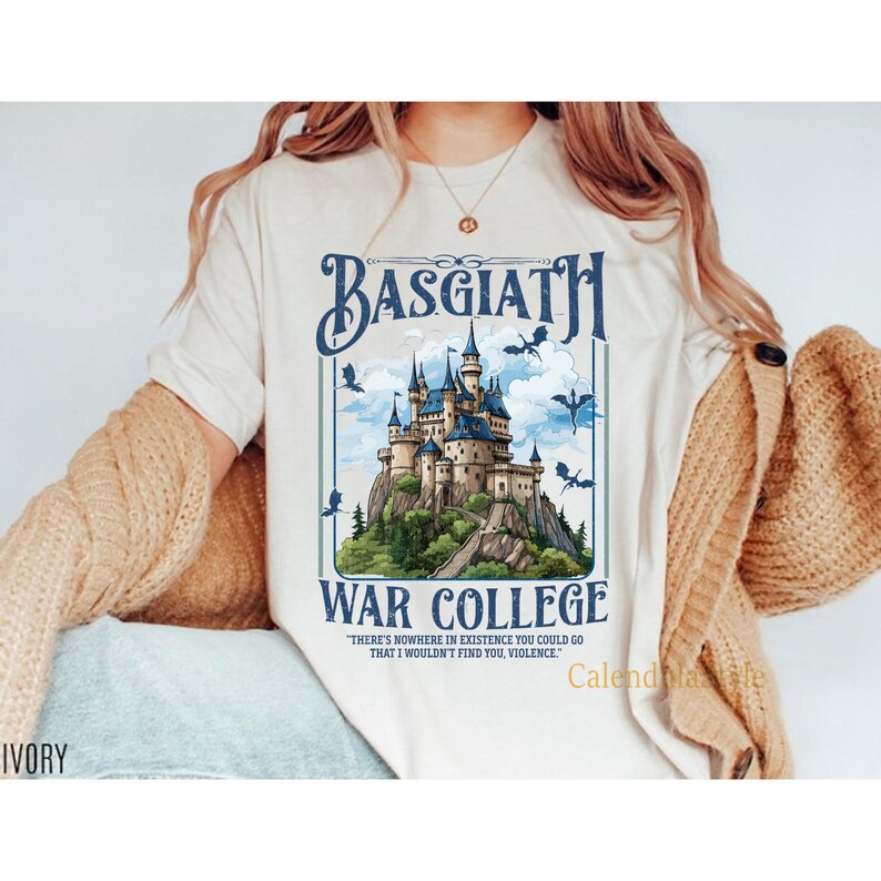 Op de afbeelding: Een wit T-shirt met een afbeelding van een kasteel met de tekst "Basgiath War College" en de quote "Er is nergens in het bestaan waar je heen kunt gaan waar ik je niet zou vinden, geweld."
