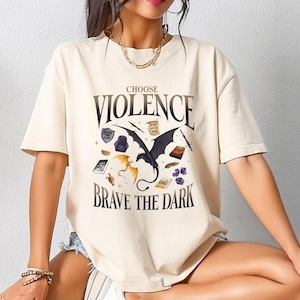 May include: A cream coloured t-shirt with a black and gold graphic of a dragon and the text "Choose Violence Brave the Dark".
