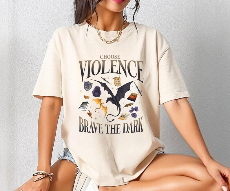 May include: A cream coloured t-shirt with a black and gold graphic of a dragon and the text "Choose Violence Brave the Dark".