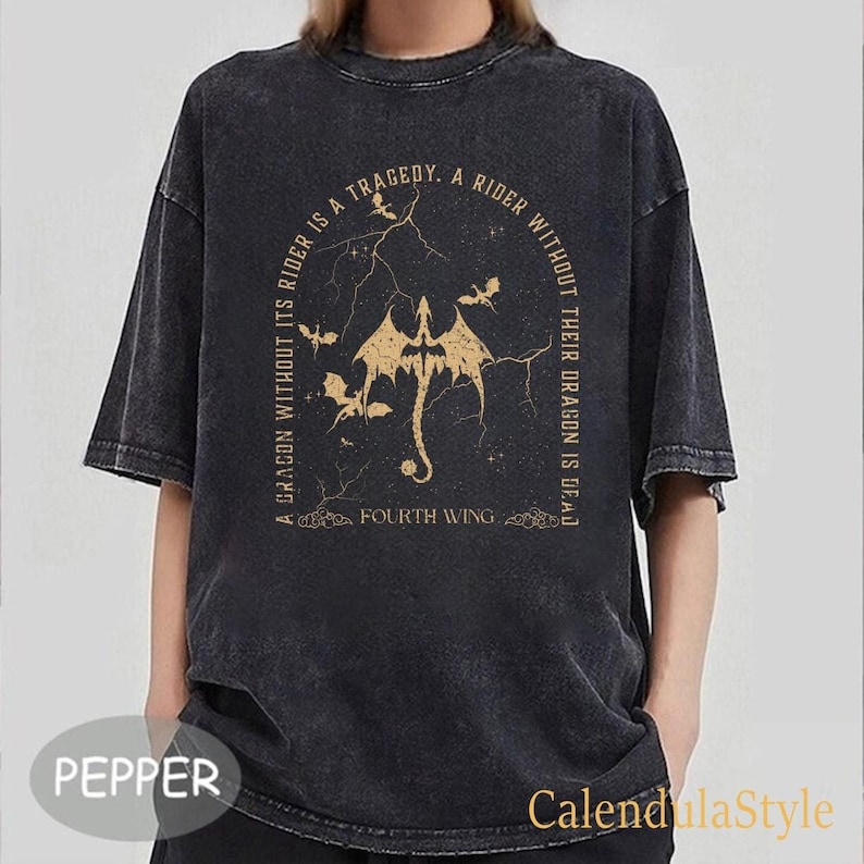 Puede incluir: Una camiseta negra con un aspecto desgastado que presenta un gr&aacute;fico dorado de un drag&oacute;n con el texto "A dragon without its rider is a tragedy. A rider without their dragon is dead. Fourth Wing."